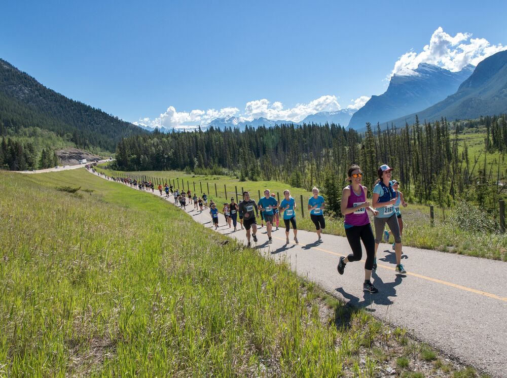 People participating in the Banff Marathon running on a trail with mountains in the background